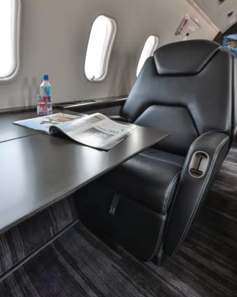 Bombardier Challenger 300 interior seat and table with a magazine and Fuji water bottle on top.