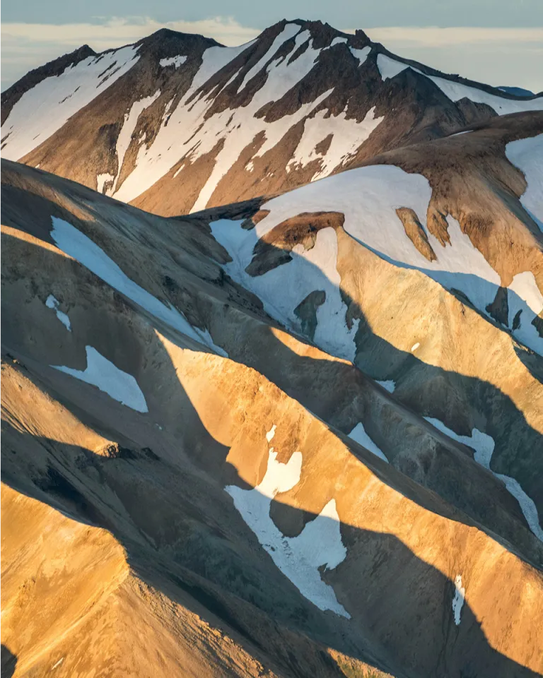 Sunlight cascades across a mountainous landscape with snow caps on top.